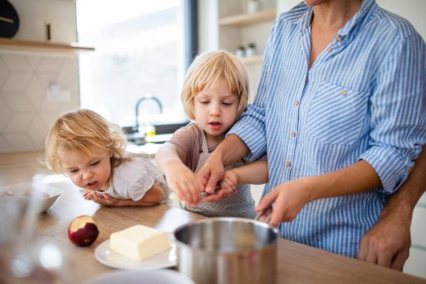 Young family with two small children indoors in kitchen, preparing food. - Foto, afbeelding
