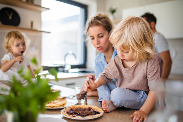 Young family with two small children indoors in kitchen, eating pancakes. - Foto, immagini