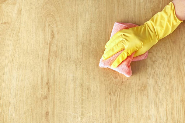 Female hand in a yellow rubber glove washes a wooden parquet floor with a pink microfiber cloth. Top view, copy space for text. - Foto, Imagen