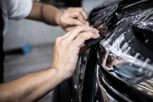 Close-up van de lak bescherming film installatie op voorbumper van moderne luxe auto. PPF is polyurethaan film aangebracht op het autooppervlak om de verf te beschermen tegen steensplinters, insectenspetters en slijtage - Foto, afbeelding