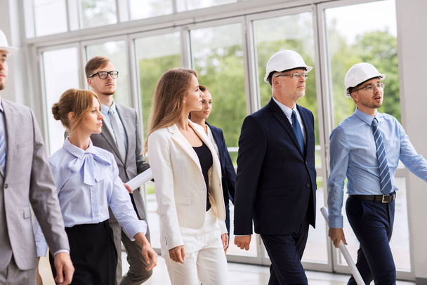equipe de negócios em capacetes andando ao longo do escritório
 - Foto, Imagem