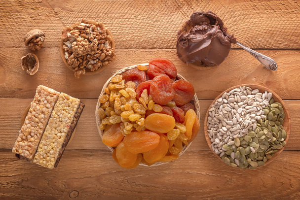 Mix of dried fruits, energy bites, chocolate paste, assorted nuts and seeds on a wooden table.Top view - Photo, Image