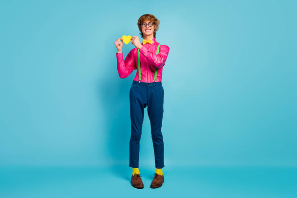 Full size photo of positive wavy hair guy hold little yellow heart show his affectionate lover romance feelings wear pink pants trousers socks isolated blue color background - Φωτογραφία, εικόνα