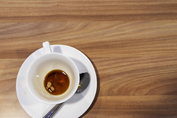 Een vieze witte koffiekop staat op een houten tafel. Restjes ontbijt. - Foto, afbeelding