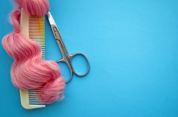 明るいピンクの髪とはさみのカールの櫛の上からの眺め。明るい青の背景で。美容室、美容室のコンセプト. - 写真・画像