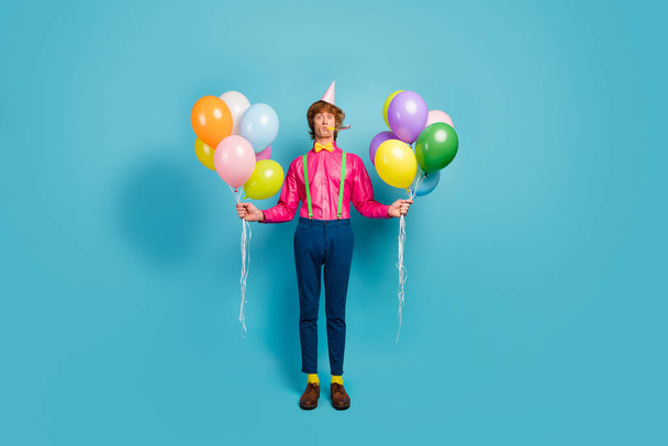 Full length photo of funky funny gentleman guy prepare anniversary party blow noisemaker hold many helium baloons wear cone headwear pink pants isolated over blue color background - Φωτογραφία, εικόνα
