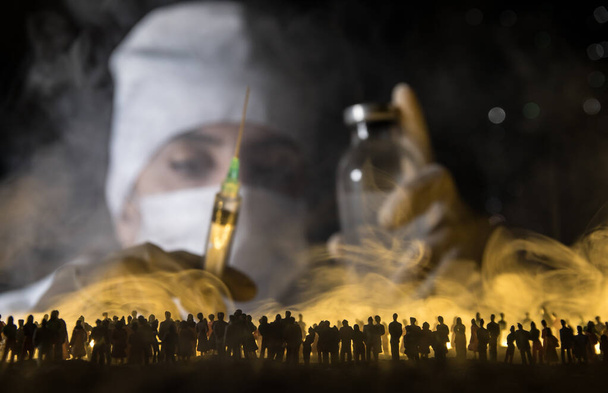 Ärztin mit Maske hält Spritze in der Hand und stellt sich gegen Menschenmenge. Virus, Ausbruch und Massenerkrankung, Coronavirus-Konzept. Selektiver Fokus. Kreative Dekoration - Foto, Bild