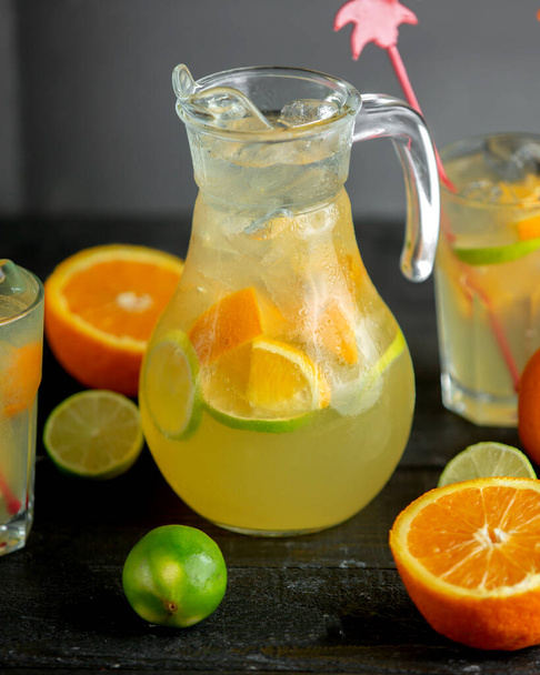 a jug of citrus beverage with orange and lime slices - Photo, Image