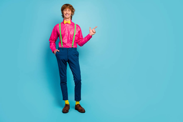 Täysikokoinen kuva positiivinen iloinen viileä kaveri promoottori kohta sormi copyspace läsnä mainoksia edistäminen osoittaa neuvoja valinta kulumista vaaleanpunainen housut kengät eristetty sininen väri tausta
 - Valokuva, kuva