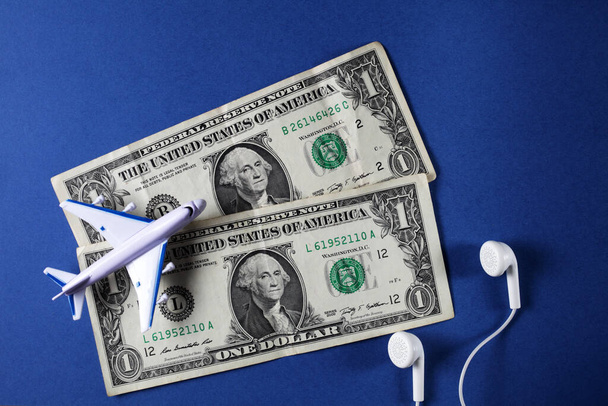 speelgoed passagiersvliegtuig op een blauwe achtergrond, dollars, koptelefoon bovenaanzicht - Foto, afbeelding