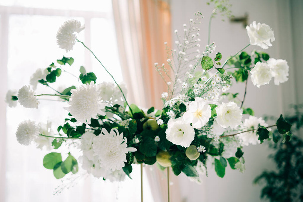 květinová výzdoba svatebních stolů, jemné bílé květy a větve čerstvé zeleně na bílém sále - Fotografie, Obrázek