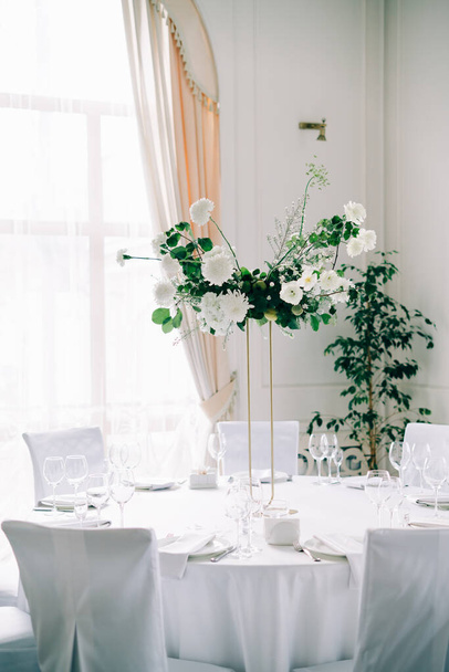 bloemdecoratie van bruiloft tafels, delicate witte bloemen en takken van vers groen op witte hal - Foto, afbeelding