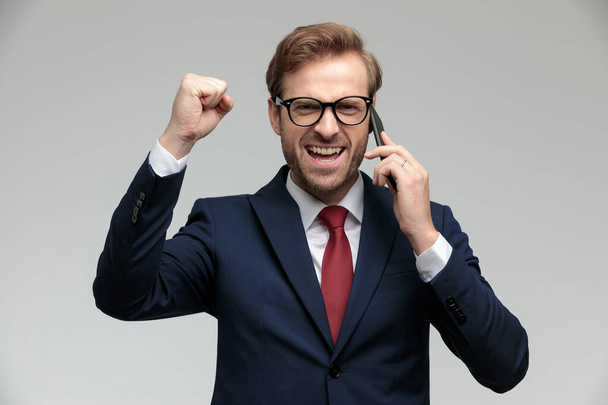 businessman standing with one fist raised while talking on phone - Photo, Image