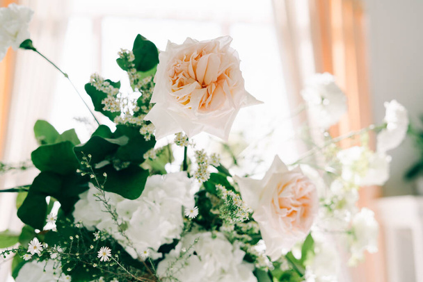 白いホールの結婚式テーブルのデザインに繊細なバラの花と新鮮な緑の美しい花の配置 - 写真・画像