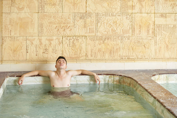 Asian Man relaxing with eyes closed enjoying hot tub alone in modern spa salon, horizontal shot - Photo, Image