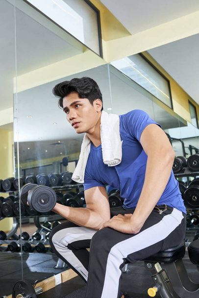 Düşük açılı çekimde, kendine güvenen genç Asyalı adam spa otelinin spor salonunda halterle egzersiz yapıyor. - Fotoğraf, Görsel