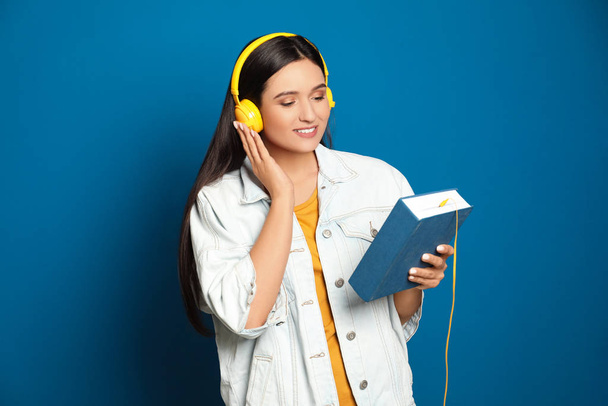 Young woman listening to audiobook on blue background - Foto, afbeelding