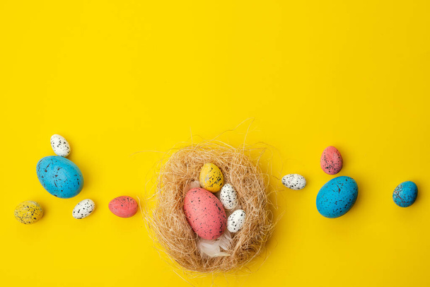 Easter background, multi-colored eggs in a nest lie on a yellow  - Photo, Image