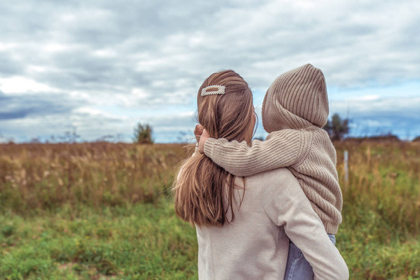 family woman mother holds her son in her arms, little boy in sweater with hood, rest in field, parenting child care love, parental support. Autumn spring day. Warm clothing. Free space for copy text. - Foto, Imagen