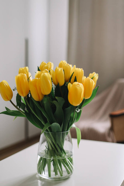 Spring flowers in living room interior. Bouquet of fresh yellow tulips on a table.  Spring or holiday concept, March 8, birthday.  - Foto, imagen