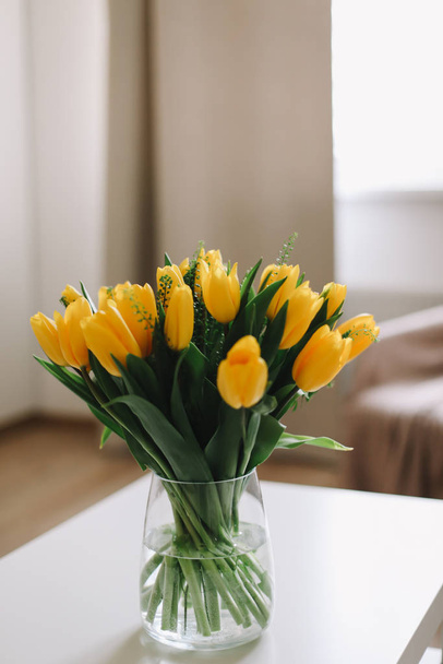 Spring flowers in living room interior. Bouquet of fresh yellow tulips on a table.  Spring or holiday concept, March 8, birthday.  - Фото, изображение