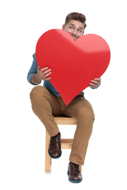 young casual man looking up and holding big red heart - 写真・画像