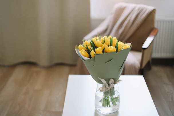 Spring flowers in living room interior. Bouquet of fresh yellow tulips on a table.  Spring or holiday concept, March 8, birthday.  - Foto, afbeelding