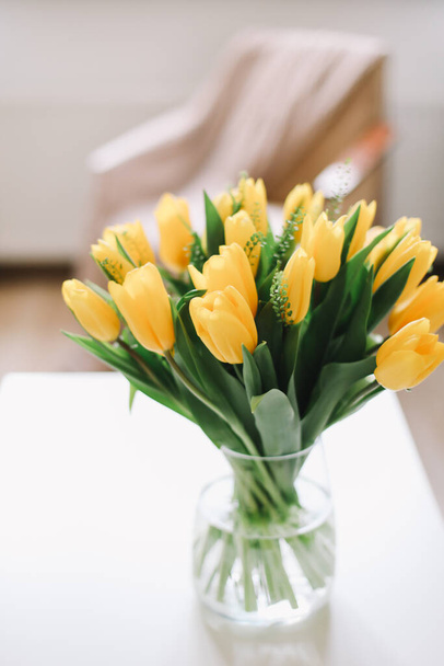 Spring flowers in living room interior. Bouquet of fresh yellow tulips on a table.  Spring or holiday concept, March 8, birthday.  - Foto, immagini