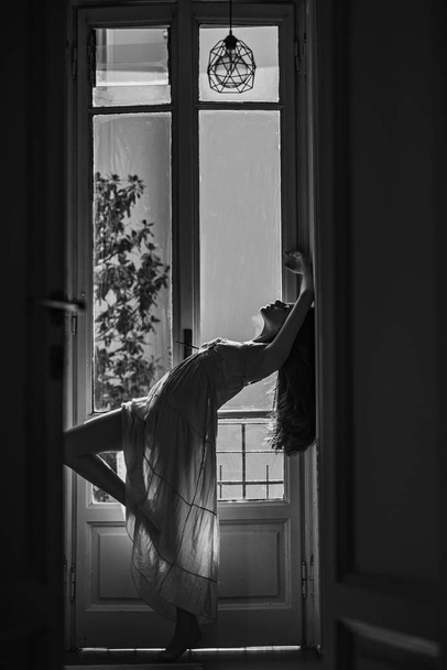 Beautiful young woman with long dark hair. Beautiful smiling woman relaxing. Morning. Sensual model girl. Sensual lady. Woman standing near the window after waking up with sunrise at morning. - Photo, Image