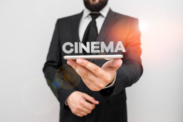 Käsiala tekstiä kirjallisesti Cinema. Käsite tarkoittaa teatteri, jossa elokuvat näytetään yleisölle viihdettä Elokuvateatteri Mies ihmisen kulumista muodollinen työpuku pidä älykäs hi tech älypuhelin käyttää yhdellä kädellä
. - Valokuva, kuva