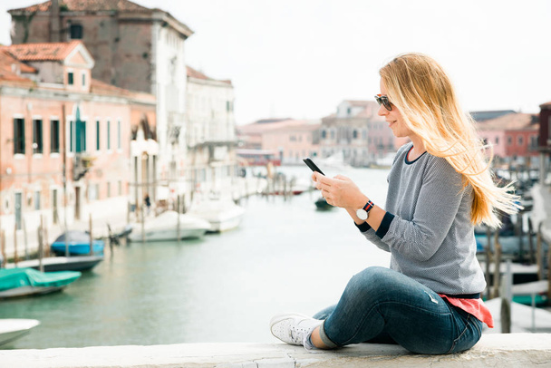 Nuori nainen matkailija älypuhelimella sillalla Muranon saarella Venetsiassa, Italiassa
 - Valokuva, kuva