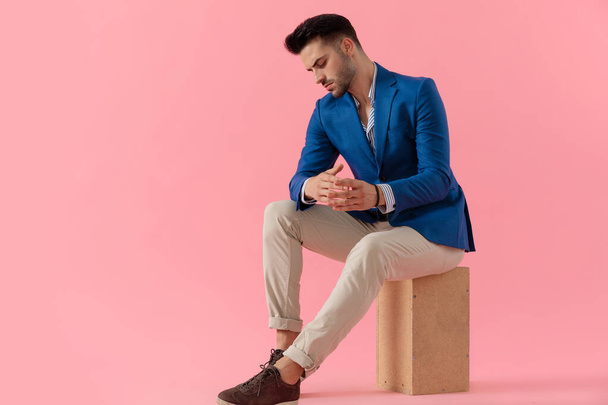 sexy young smart casual man sitting on a wooden box - Fotó, kép