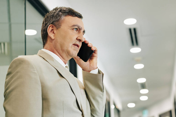 Horizontale lage hoek borst omhoog portret van middelbare leeftijd blanke zakenman praten op de telefoon - Foto, afbeelding