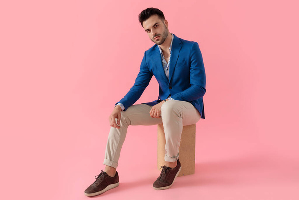 sexy smart casual guy holding elbow on knee in a fashion pose - Φωτογραφία, εικόνα