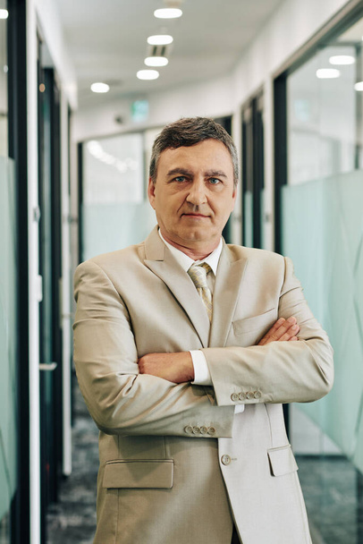 Vertical medium portrait of successful middle-aged man wearing suit standing with arms crossed looking at camera - Foto, afbeelding