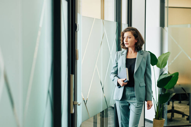 Beautiful mature businesswoman walking along office business corridor looking way, horizontal shot - Valokuva, kuva