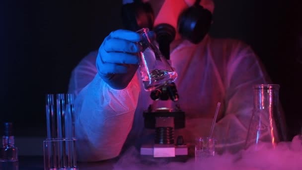 scientist biologist or chemist in laboratory neon light shakes transparent liquid in beaker.Liquid nitrogen floats on equipment table. laboratory experiments with cryogen and nitrogen. Lab equipment. - Footage, Video