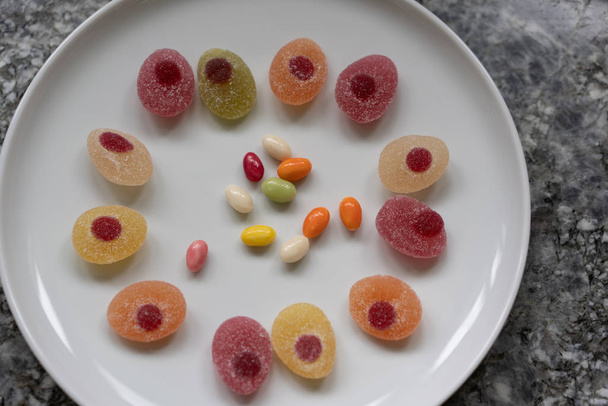 Sweeties for easter. Easter candies in a circle on a white plate on a gray granite table. - Фото, изображение