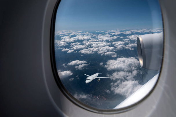 Самолет пролетает сквозь облачное небо в окне другого реактивного самолета
 - Фото, изображение