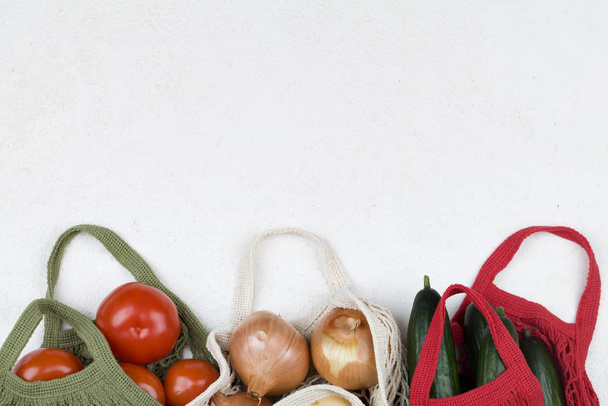 Shopping bag in rete bianca, verde e rossa con pomodori rossi, fiocco e cetrioli verdi su sfondo bianco
. - Foto, immagini
