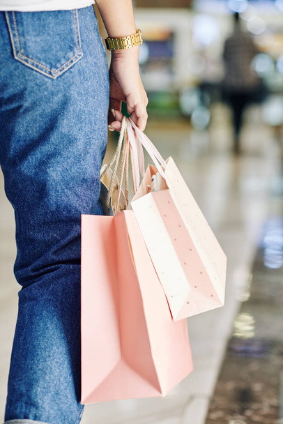 Femme méconnaissable portant un jean marchant le long du centre commercial avec des sacs à provisions en papier, plan vertical
 - Photo, image