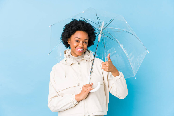 Mladá africká americká žena drží deštník izolovaný úsměv a zvedá palec nahoru - Fotografie, Obrázek
