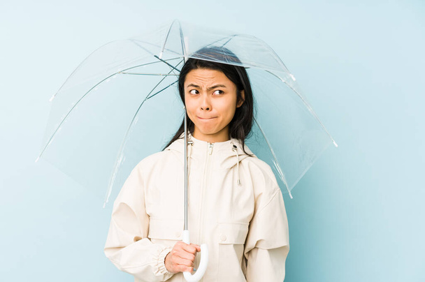 Young chinese woman holding an umbrella isolated excited keeping ok gesture on eye. - Фото, зображення