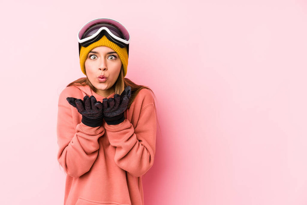 Mulher branca jovem vestindo uma roupa de esqui lábios dobráveis isolados e segurando palmas para enviar beijo de ar
. - Foto, Imagem