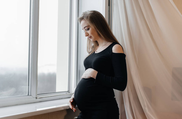 A pregnant girl is breathing fresh air from the window - Фото, зображення