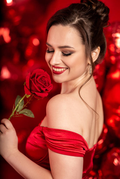 Piękna młoda kobieta w czerwonej sukni wieczorowej pozowanie na czerwonym tle z dużym kształcie serca balony.  - Zdjęcie, obraz