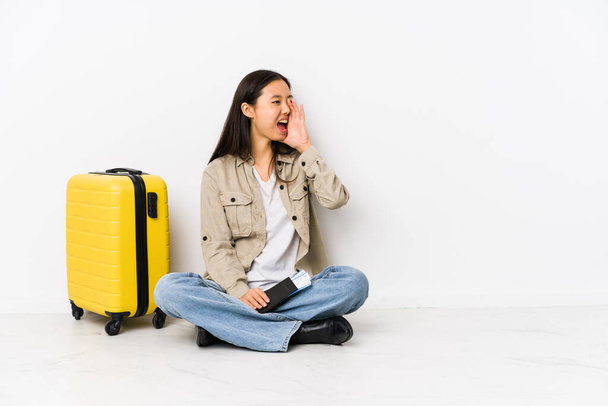 Jovem chinesa viajante mulher sentado segurando um cartão de embarque gritando e segurando palma perto da boca aberta
. - Foto, Imagem