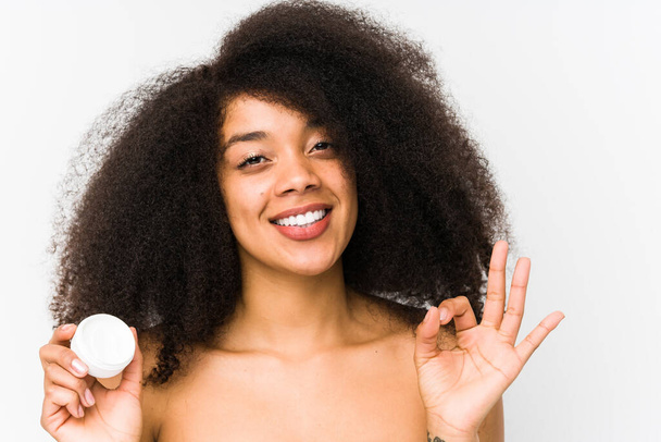 Jonge afro vrouw met een vochtinbrengende crème geïsoleerd vrolijk en vol vertrouwen tonen ok gebaar. - Foto, afbeelding