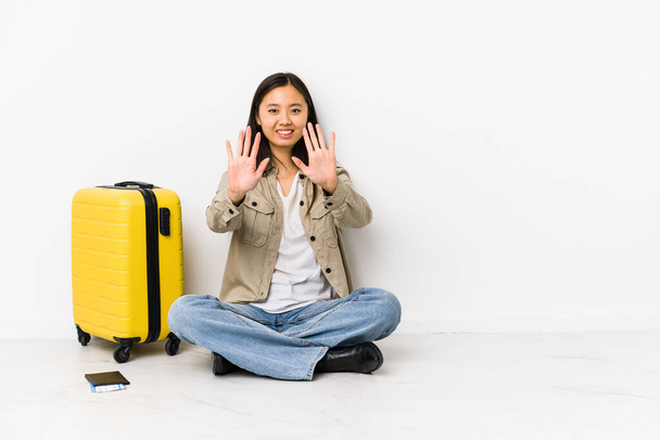 Joven viajera china sentada sosteniendo una tarjeta de embarque que muestra el número diez con las manos
. - Foto, Imagen