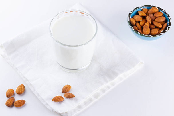 Almond milk with almond on white background. Organic almond milk in a glass for healthy breakfast. Vegan milk from almonds nuts on a white napkin. Alternative milk - Фото, изображение